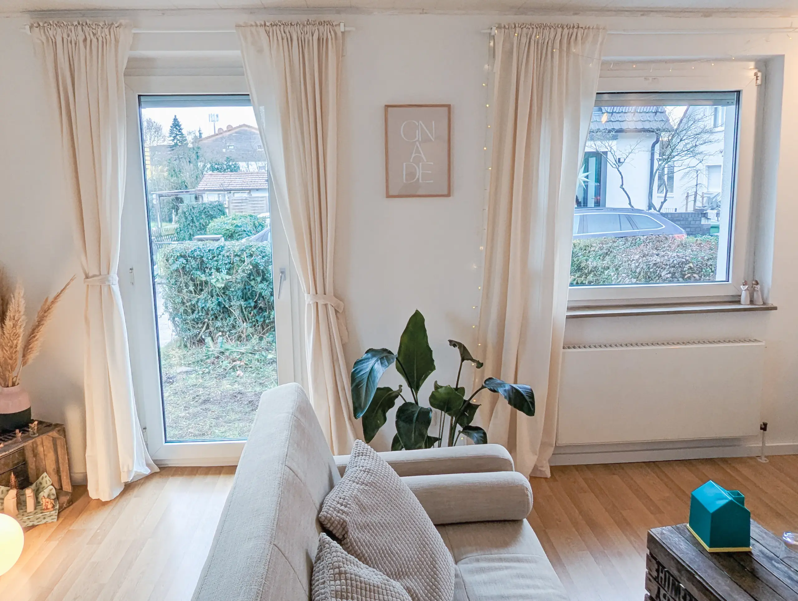 Helles Wohnzimmer mit großen Fenstern, Sofa und Pflanzen in gemütlicher Atmosphäre.