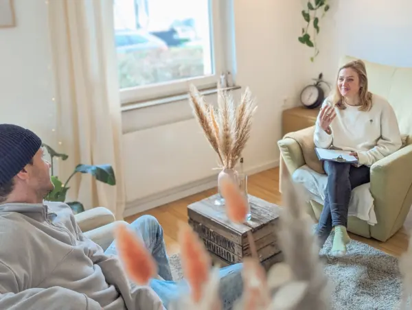 Psychotherapie-Sitzung in hellem Wohnzimmer mit Therapeutin und Klient.
